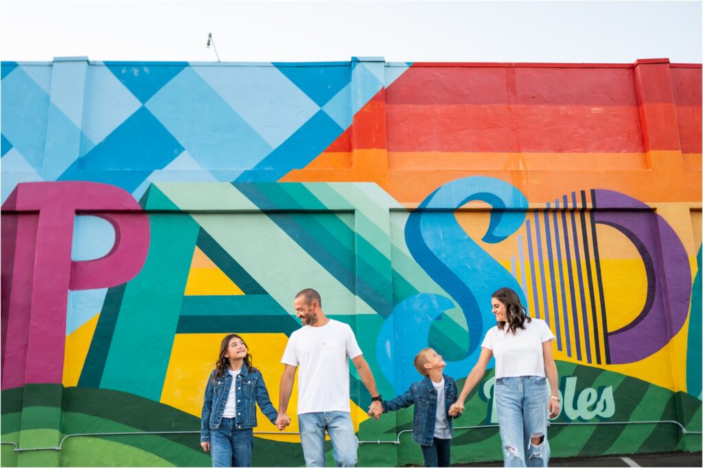 Family walking near a colorful mural in Downtown Paso Robles at sunrise during a family photo session